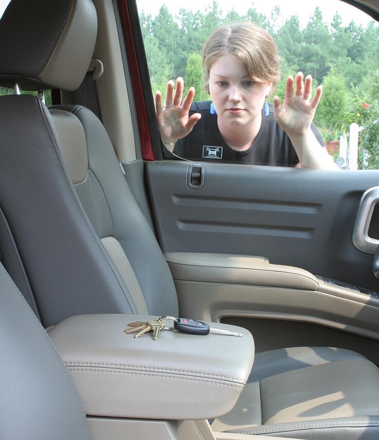 A woman looking through her car window at the keys she left on the driver's seat.
